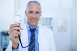 Happy doctor smiling at camera and showing his stethoscope